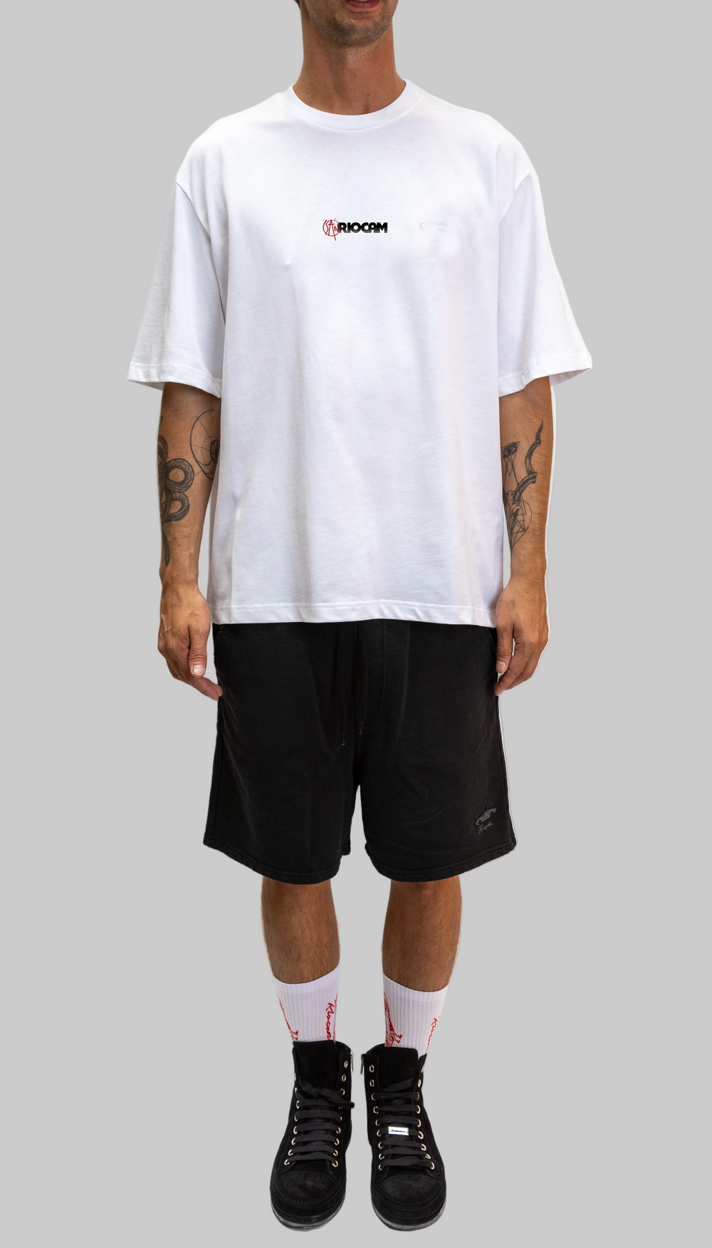 Person wearing a white t-shirt with a logo and black shorts on a white background
